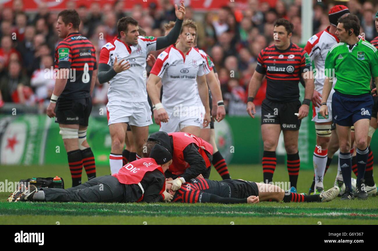 Alex Goode von Saracens liegt auf dem Spielfeld und erhält medizinische Hilfe nach einer Kollision mit Ulsters Jared Payne (weißes Trikot, Hände in der Luft) während des Heineken Cup Quarter Final Match im Ravenhill Stadium, Belfast. Stockfoto