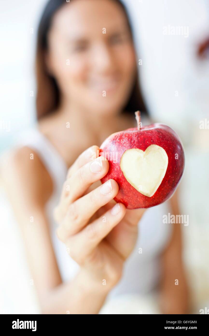 -MODELL VERÖFFENTLICHT. Junge Frau hält einen Apfel mit einer Herzform. Stockfoto