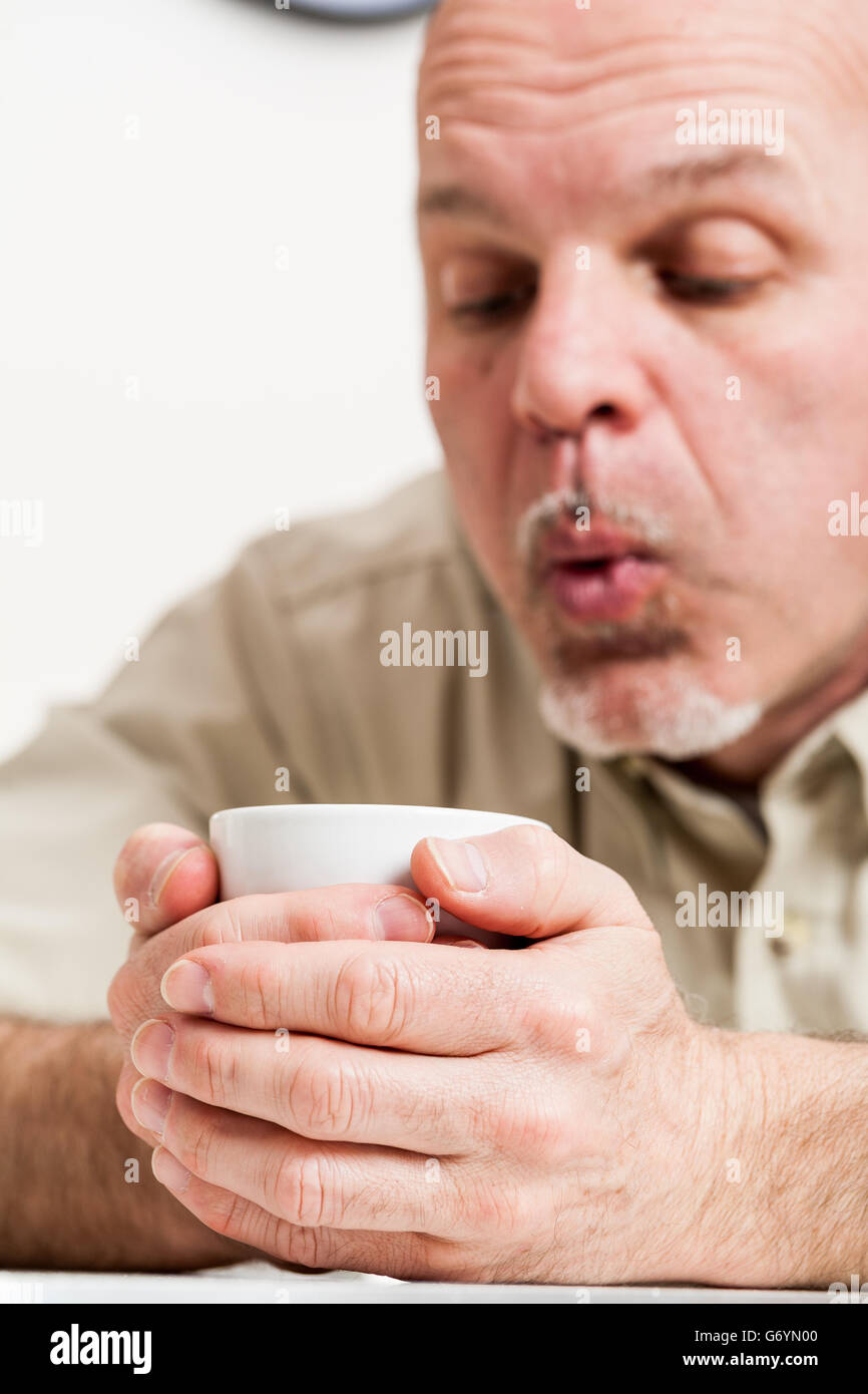 Beschnitten, Kopf und Schultern des reifen Mannes Einblasen in kleinen weißen Teetasse in Händen Stockfoto
