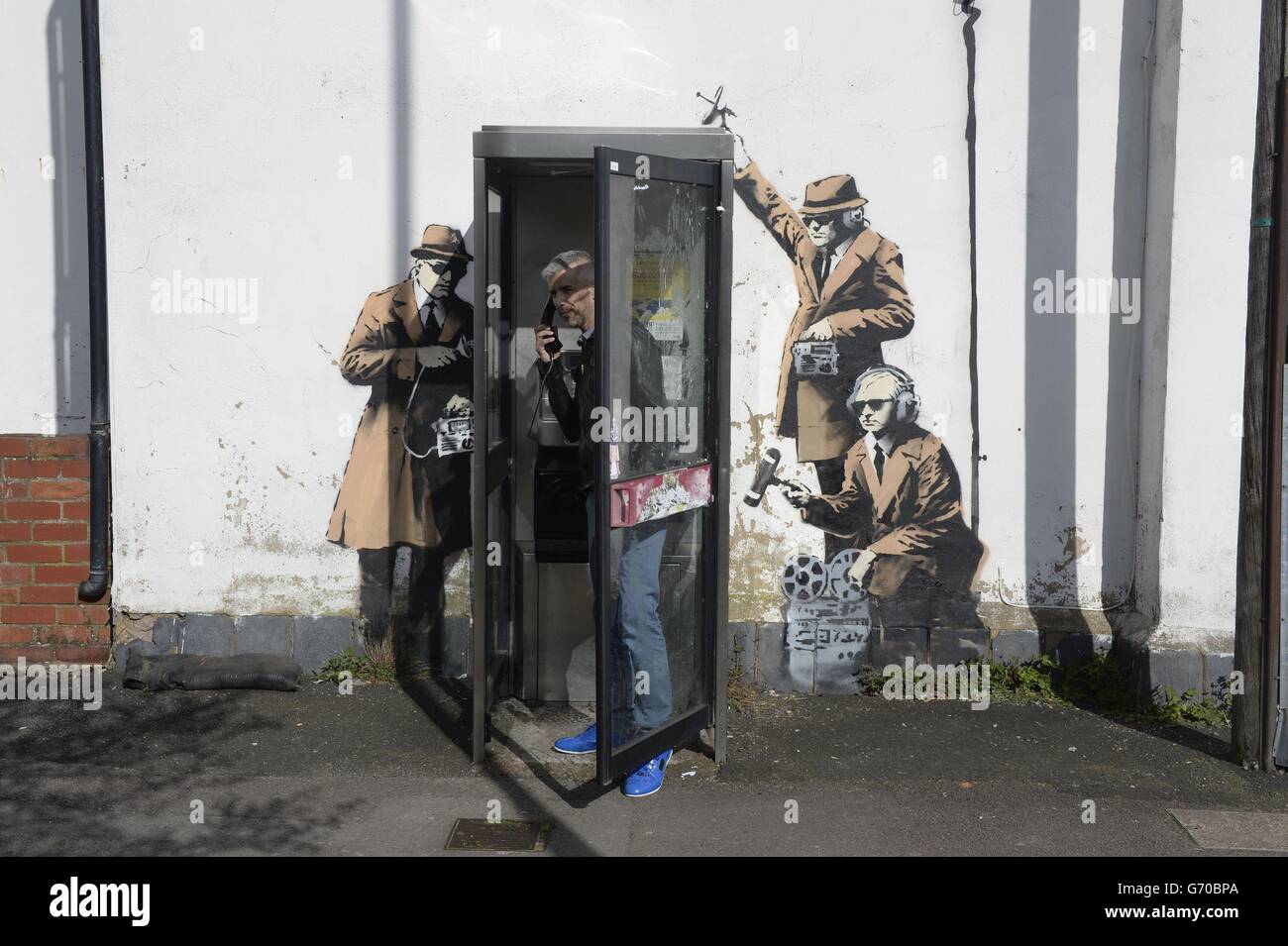 Das neue Graffiti-Street-Art-Stück, das im Verdacht steht, ein Banksy zu sein, erschien an der Seite eines Hauses in der Fairview Road neben der St. Anne's Terrace in Cheltenham. Das Kunstwerk, das drei Figuren zeigt, die an einer Telefonbox in ein Gespräch hineinhören, ist nur wenige Kilometer von Government Communications Headquaters (GCHQ) entfernt, das für die Bereitstellung von Signalinformationen und Informationssicherheit an die britische Regierung und die Streitkräfte verantwortlich ist. Stockfoto