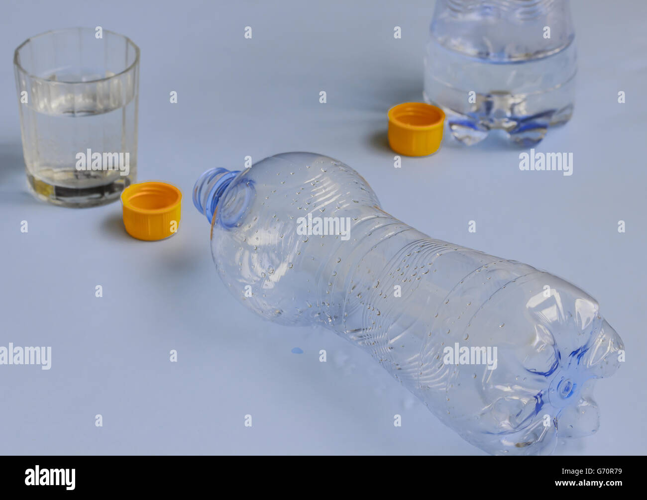 zwei Flaschen Wasser abgelassen, orangefarbene Kappe und das Glas Stockfoto
