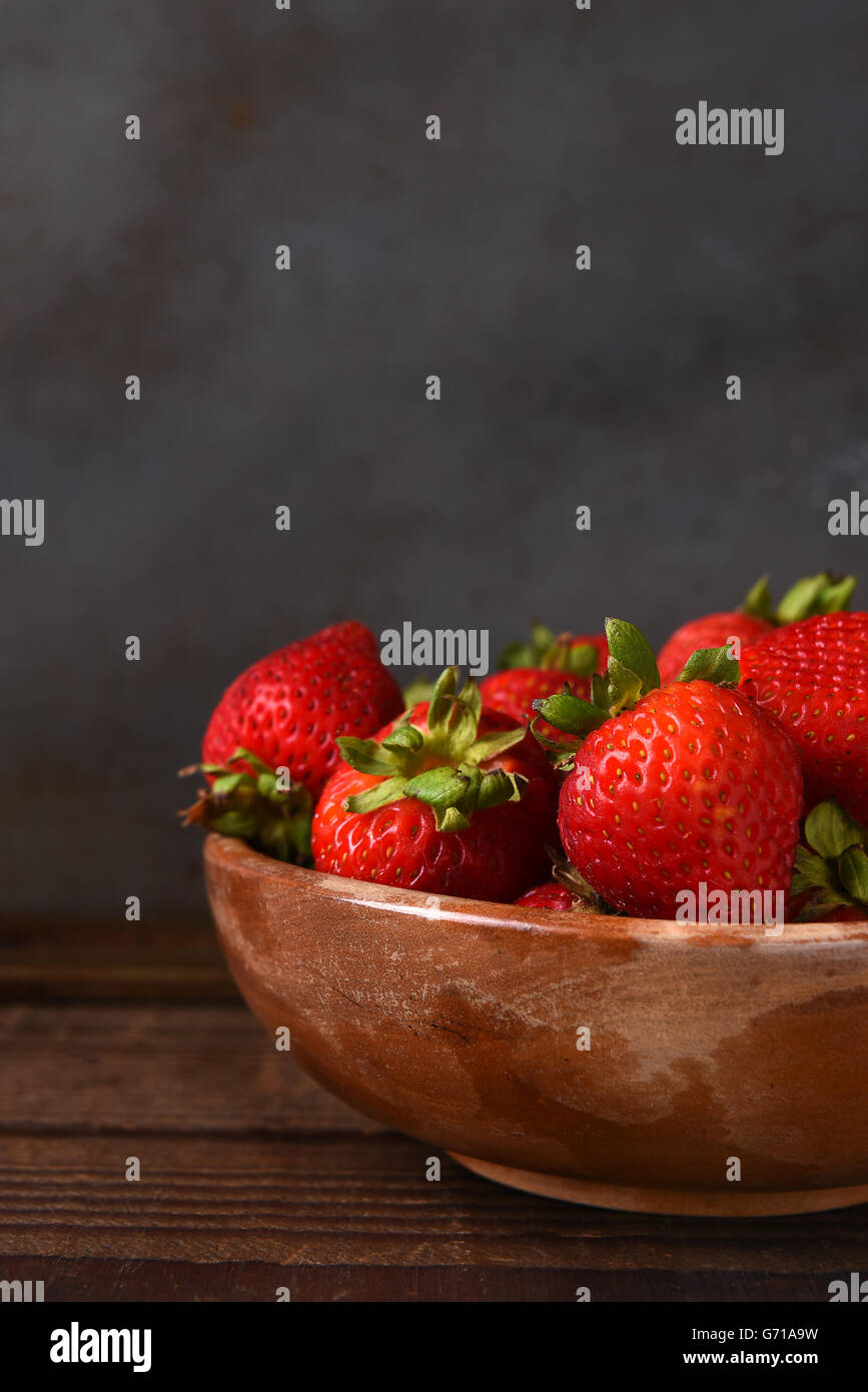 Stillleben mit einer Schüssel voll von frisch gepflückten Erdbeeren auf einem Holztisch. Hochformat mit Textfreiraum. Stockfoto