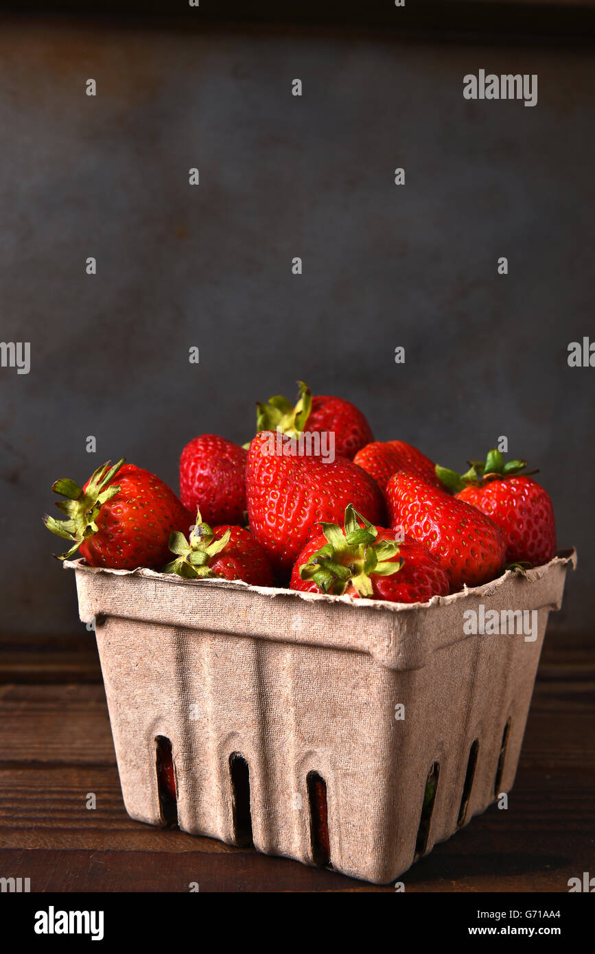 Stillleben mit der Pappe fertigen Container voll mit frisch gepflückten Erdbeeren auf einem Holztisch. Hochformat mit Textfreiraum. Stockfoto