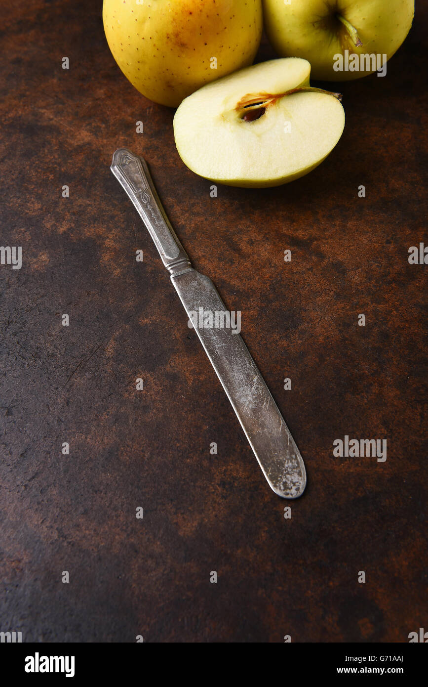 Nahaufnahme von einem alten Messer mit goldenen Äpfel im Hintergrund. Hochformat auf eine dunkle gesprenkelte Oberfläche. Stockfoto