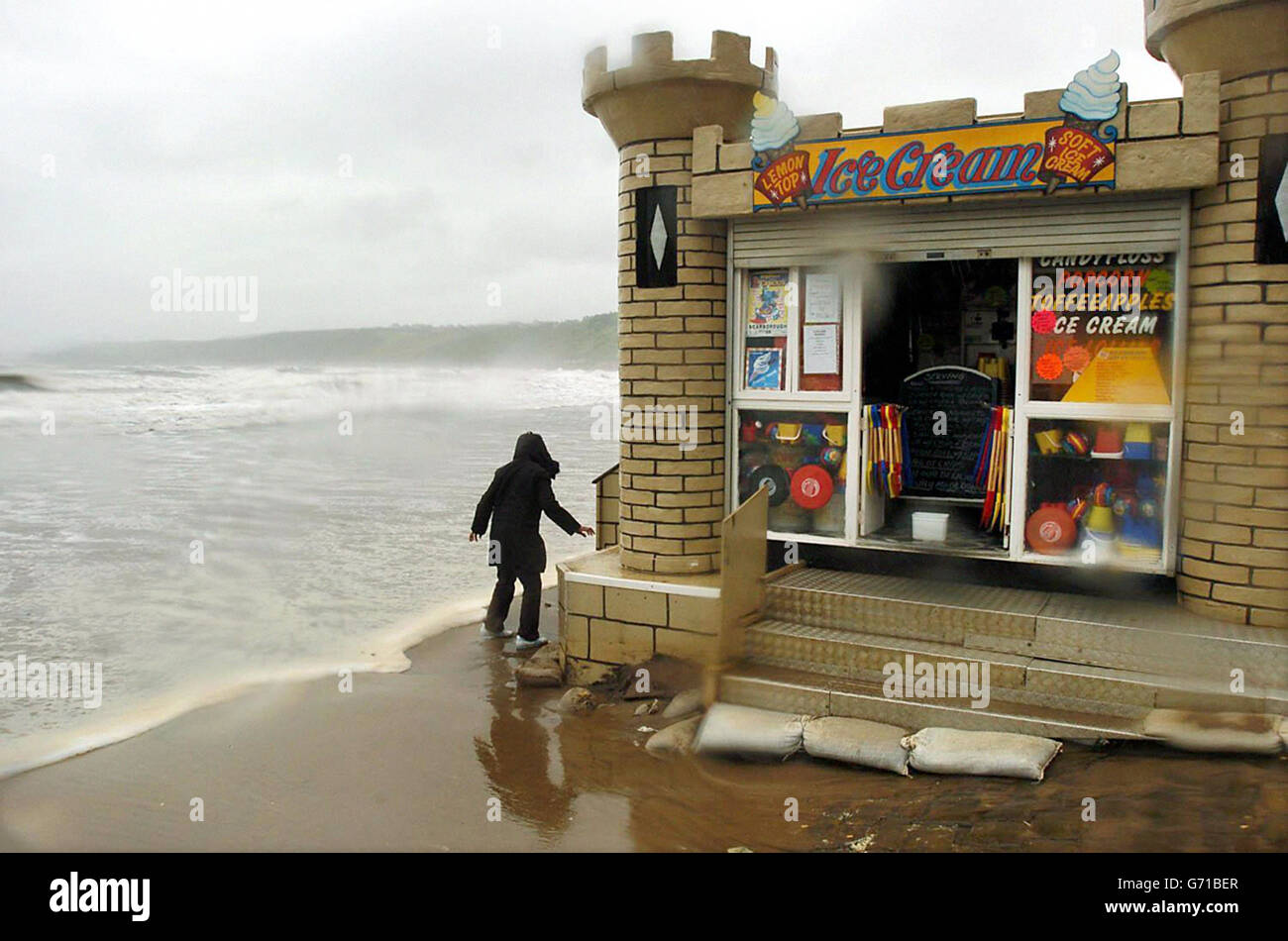 Eine Ladenbesitzerin stapelt Sandsäcke, um ihre Räumlichkeiten zu schützen, während Sturmwind, Flut und sintflutartiger Regen den Strand von Scarborough überfluten. Während sich Großbritannien von einigen der schlimmsten Sommerstürme erholt, die es je gab, waren Tausende von Häusern immer noch ohne Strom. Stockfoto