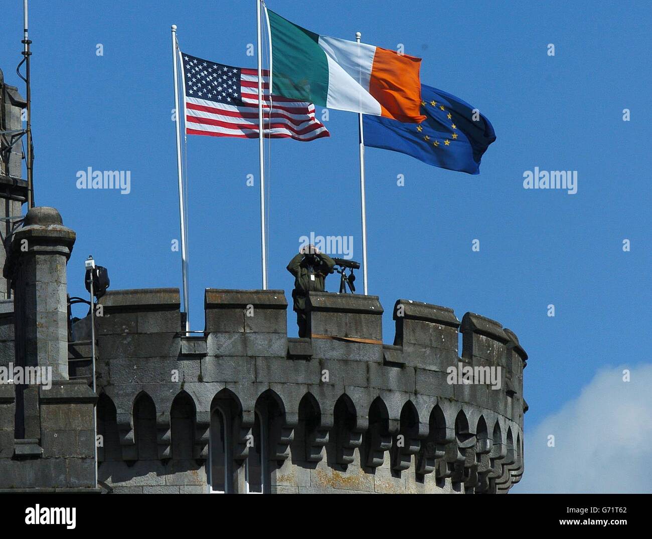 Die Flaggen der USA, Irlands und der EU fliegen über Dromoland Castle, County Clare, Irland, während ein Offizier die umliegende Landschaft beobachtet. Stockfoto