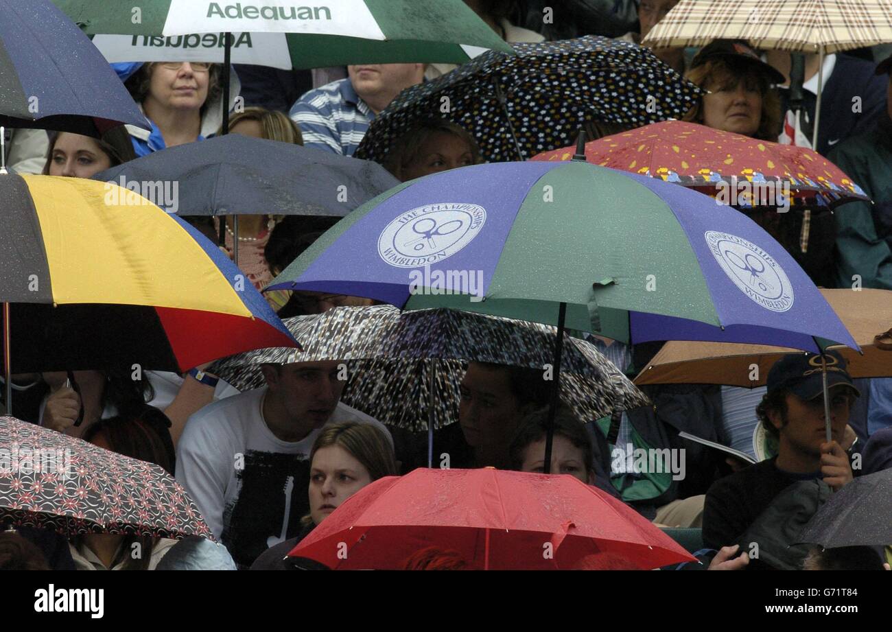 Tennis-Fans schützen sich vor dem Regen auf dem Center Court bei den Lawn Tennis Championships in Wimbledon. Der Spielbeginn wurde wegen der Duschen verzögert. KEIN HANDY Stockfoto