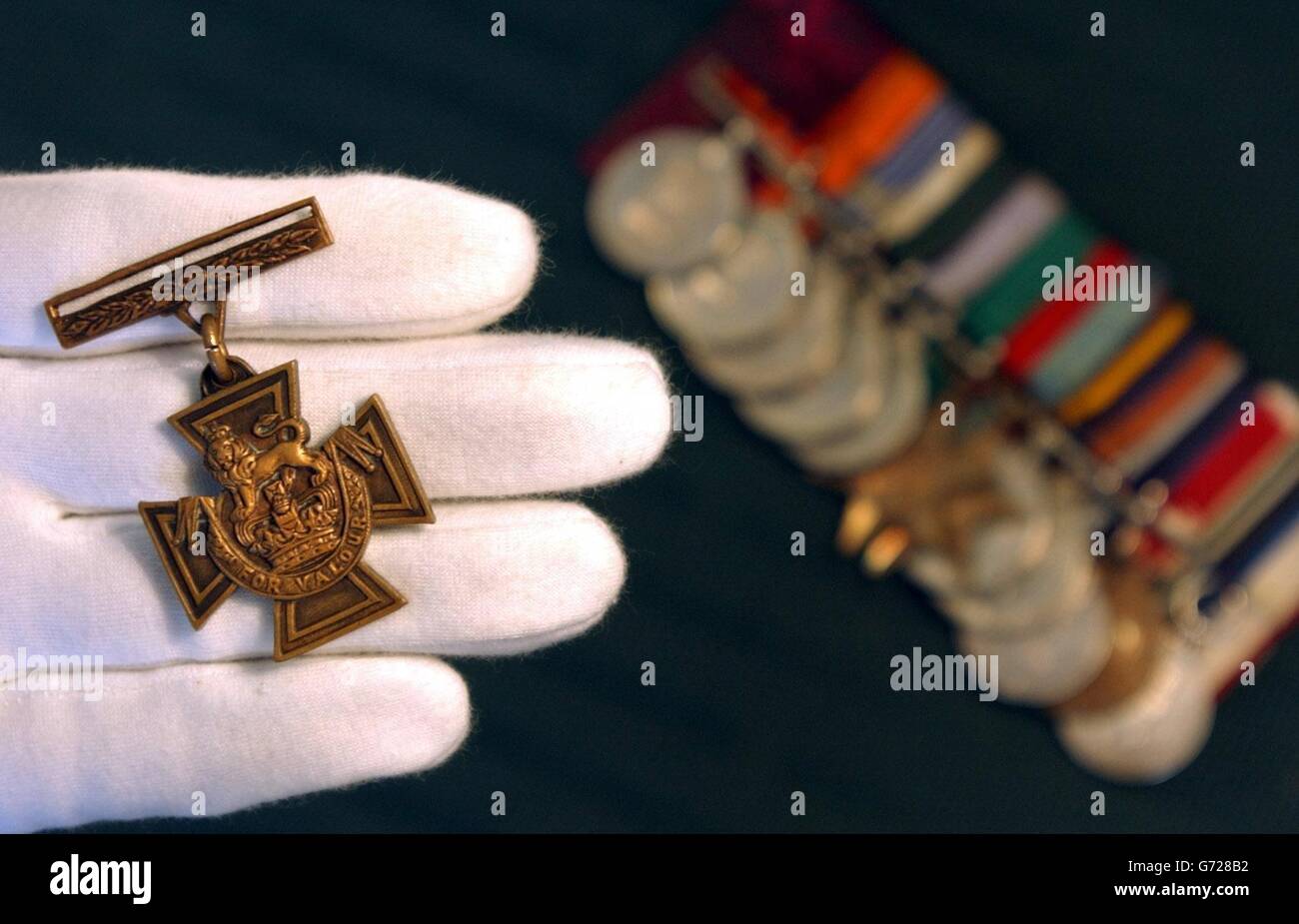 Ein Spink-Mitarbeiter hält das Victoria-Kreuz, das am Dienstag, 6. Juli 2004, dem Ehrenhauptmann Agansing Rai (links) der 5. Royal Gurkha Gewehre im Zentrum von London für "Unbeugsamen Mut" verliehen wurde. Die Medaille, die Kapitän Rai nach einer Schlacht in Burma im Jahr 1944 verliehen wurde, wird voraussichtlich 110,000 - 130,000 erhalten, wenn sie von Spink am 22. Juli als Teil von Kapitän Rais Satz von 13 Medaillen verkauft wird. Stockfoto