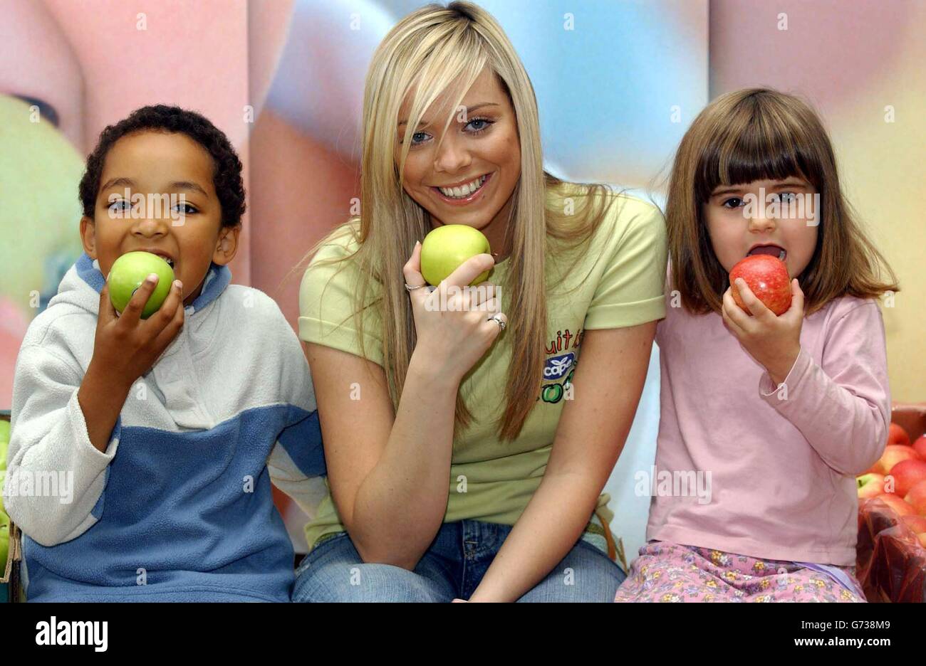 Die Ex-Atomic Kitten Liz McClarnon posiert mit den Schulkindern Airton da Silva, 7, (links) und Connie ward, 6, während einer Fotoaktion an der Ashmead School in Südlondon beim Start der Kampagne „Fruit is Cool“, die von Cape Apples gesponsert wird, um gesunde Ernährung bei 7- bis 16-Jährigen zu fördern. Untersuchungen von Cape haben ergeben, dass Kinder fast die Hälfte ihres Monatseinkommens für Süßigkeiten, Chips und Schokolade ausgeben. Stockfoto