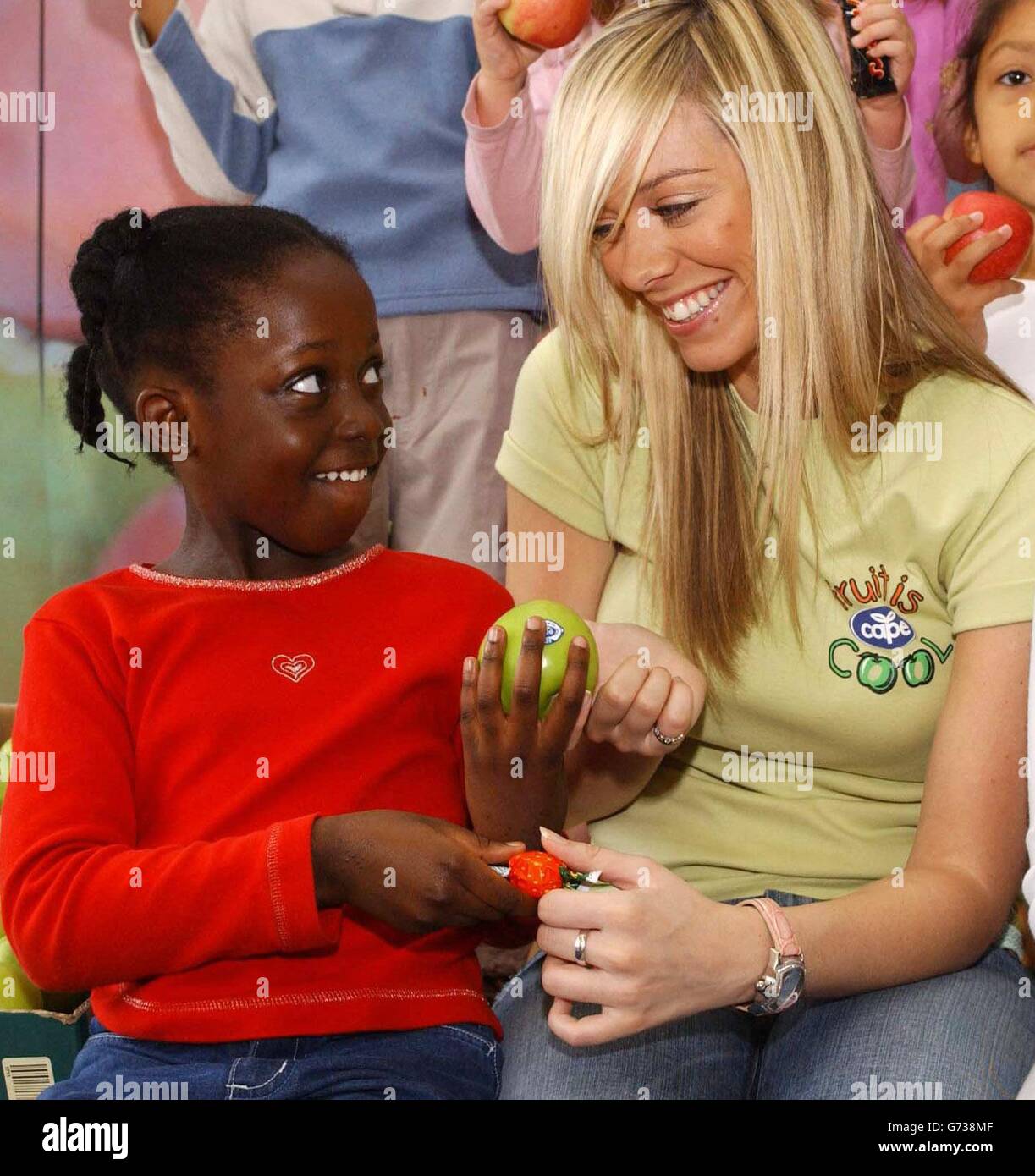 Die Ex-Atomic Kitten Liz McClarnon und die 7-jährige Denise Tetteh während einer Fotoaktion an der Ashmead School in Südlondon beim Start der Kampagne „Fruit is Cool“, die von Cape Apples gesponsert wurde, um eine gesunde Ernährung bei den 7- bis 16-Jährigen zu fördern. Untersuchungen von Cape haben ergeben, dass Kinder fast die Hälfte ihres Monatseinkommens für Süßigkeiten, Chips und Schokolade ausgeben. Stockfoto