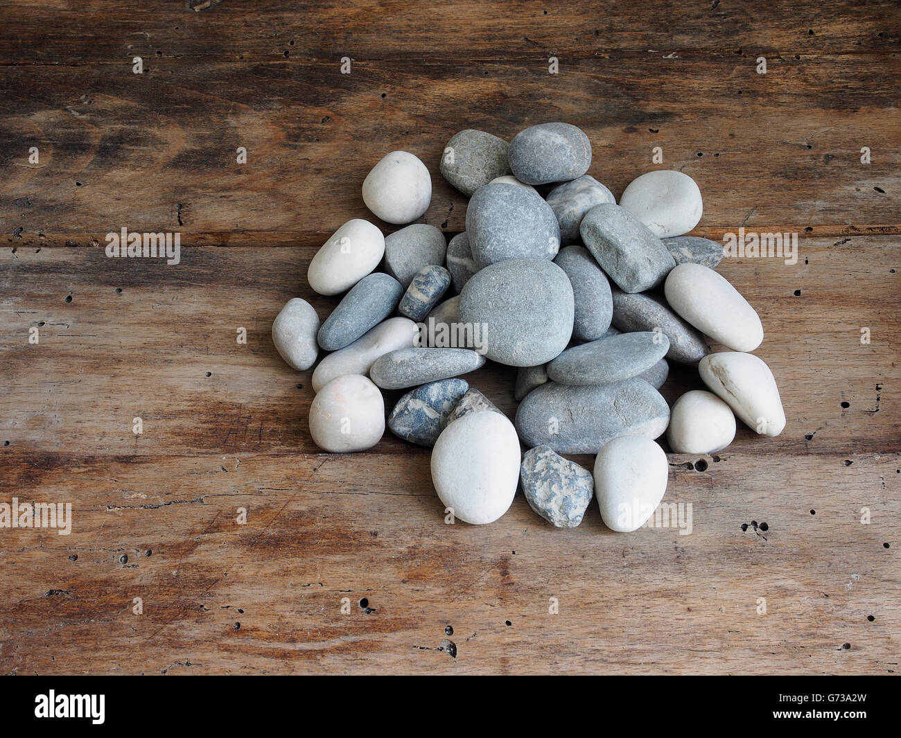 Gruppe von grauen Steinen auf einem Holztisch mit kleinen Löchern, die durch Holzwürmer gemacht. Stockfoto