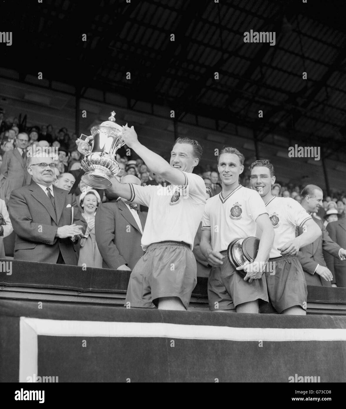 NAT Lofthouse, Mitte-vorne und Kapitän von Bolton Wanderers, hält den FA Cup triumphierend hoch, nachdem er ihn vom Duke of Edinburgh in Wembley erhalten hat. Bolton besiegte Manchester United mit 2:0. Stockfoto
