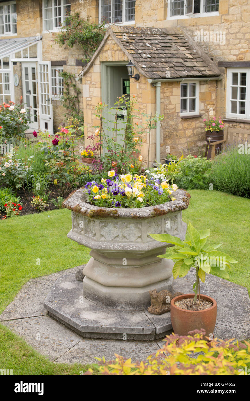 Stein-Urne voller Blumen draußen in einem Cotswold Cottage-Garten. Cotswolds, England Stockfoto