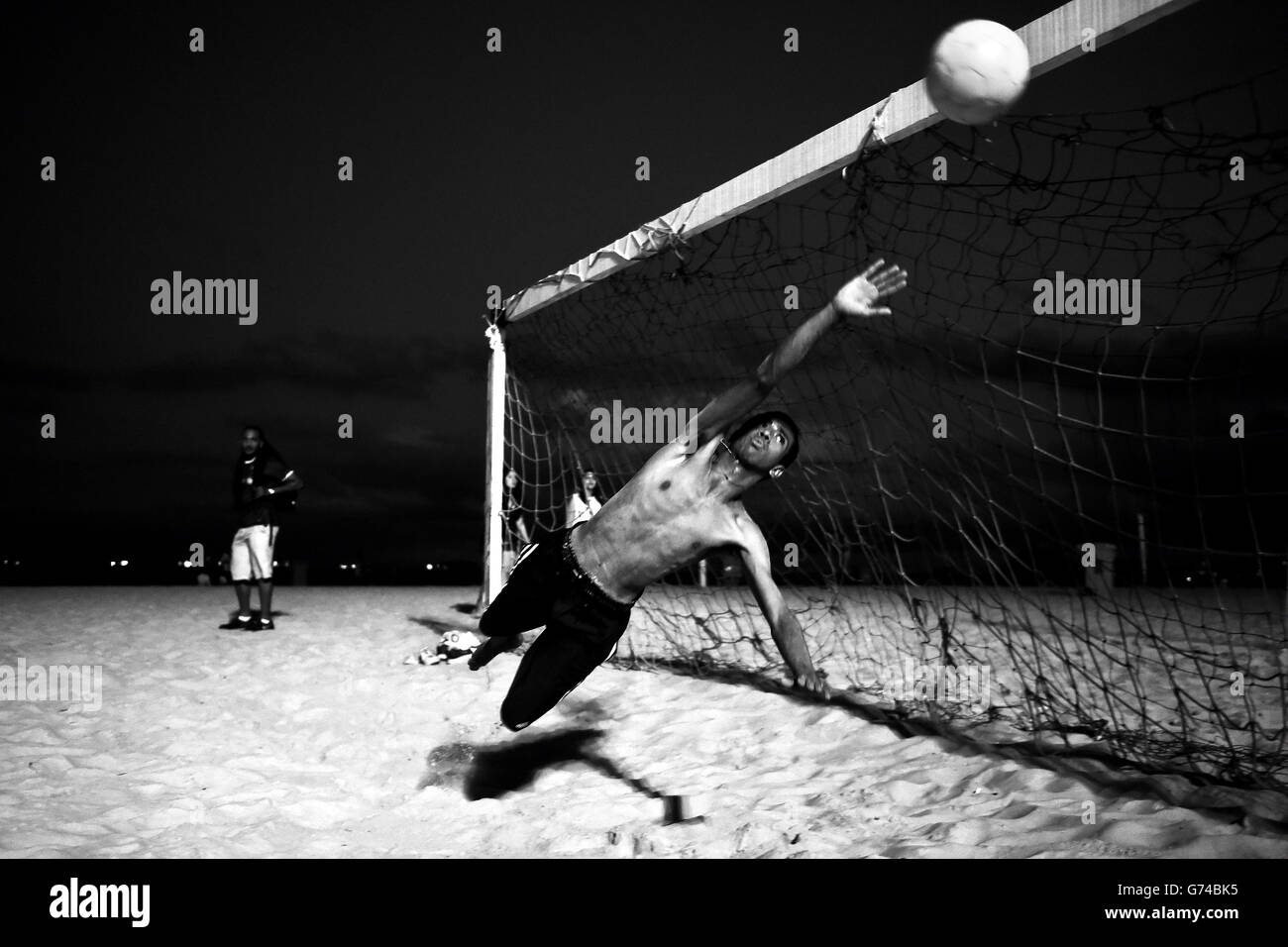 Ein brasilianischer Junge spielt Fußball unter Flutlicht am Strand von Coabba in Rio de Janeiro Stockfoto