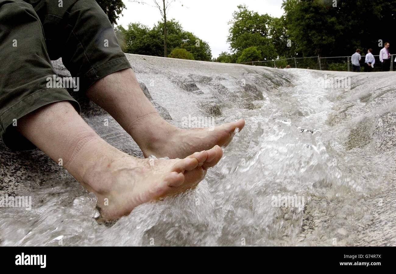 Ein Mann kühlt seine Füße, während Wasser durch den Diana Memorial Fountain im Hyde Park im Zentrum von London fließt. Der Brunnen, der seit seiner Enthüllung unter einer Reihe von Kinderkrankheiten litt, soll am 20. August wieder für die Öffentlichkeit zugänglich gemacht werden. Stockfoto