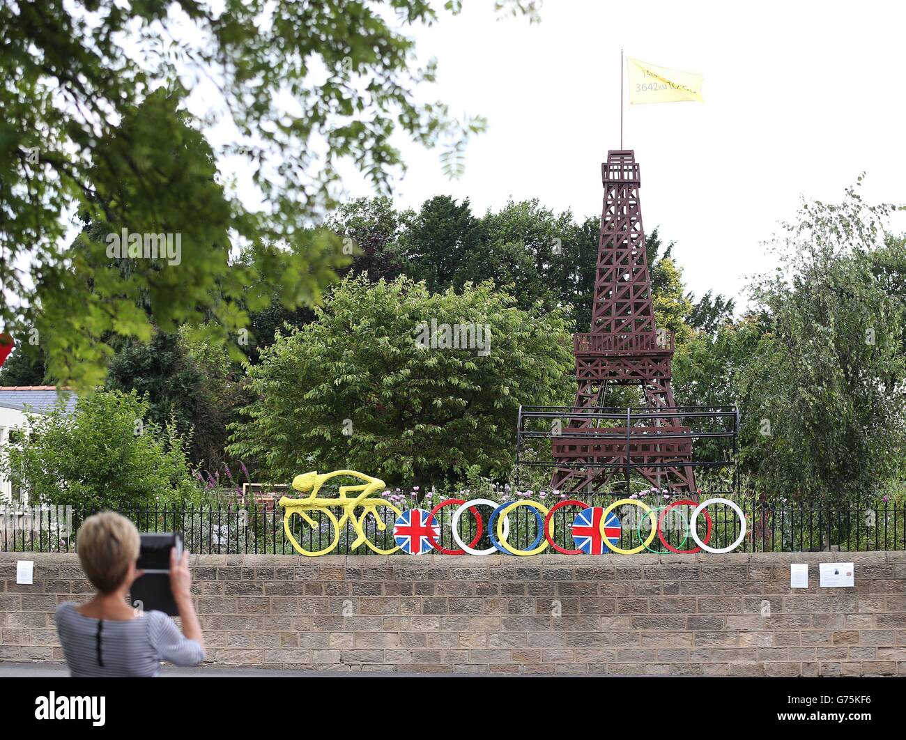 Radfahren - Tour de France Previews - Tag drei. Eine Frau fotografiert eine 7,5 m hohe (plus Fahnenstange) Nachbildung des Eiffelturms in Burley in Wharfedale. Stockfoto