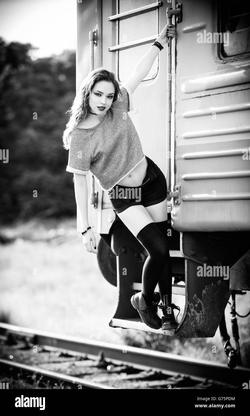 Outdoor gedreht: lächelnde junge Rock Mädchen in kurzen Hosen, Hemd und Gamaschen steht in der Nähe der Eisenbahnwaggon. Schwarz / weiß Stockfoto
