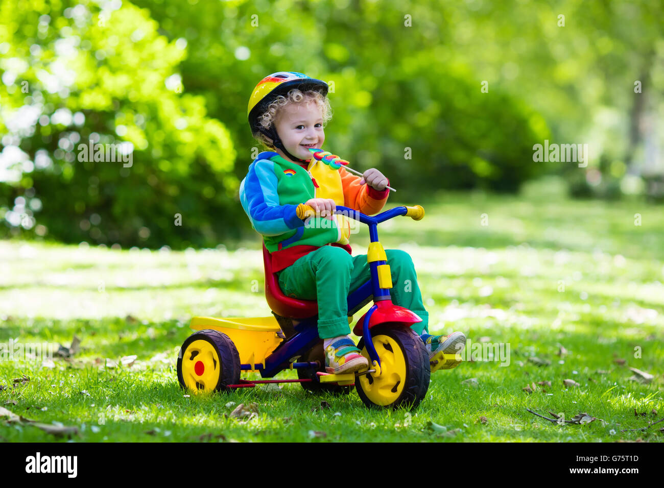 Süsser Boy tragen Schutzhelm sein Dreirad im sonnigen Park fahren. Kinder Fahrrad. Erstes Fahrrad für kleines Kind. Stockfoto