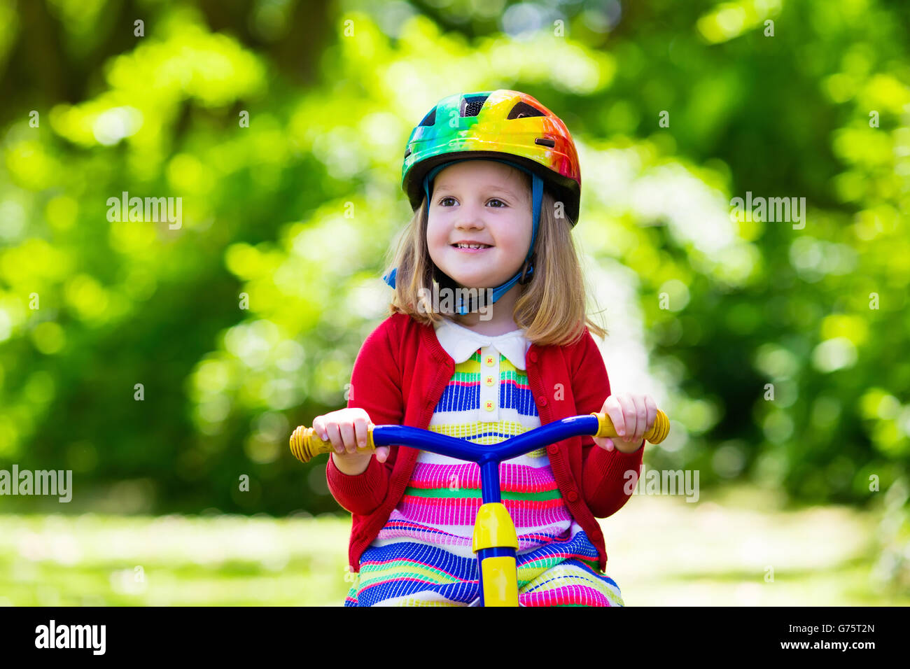 Süsser Boy tragen Schutzhelm sein Dreirad im sonnigen Park fahren. Kinder Fahrrad. Erstes Fahrrad für kleines Kind. Stockfoto