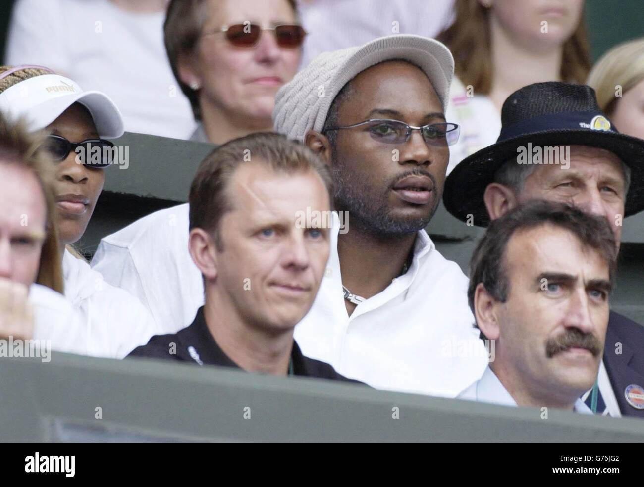 KEINE KOMMERZIELLE NUTZUNG. Großbritanniens schwergewichtige Boxmeisterin Lennox Lewis (in weißem Hut) sitzt mit Serena Williams (links), während sie der Titelverteidigerin Venus Williams in Wimbledon beim Spielen der jungen, hoffnungsvollen britischen Tennismeisterin Jane O'Donoghue zusehen. Williams schlug O'Donoghue in geraden Sätzen 6:1/6:1. Stockfoto