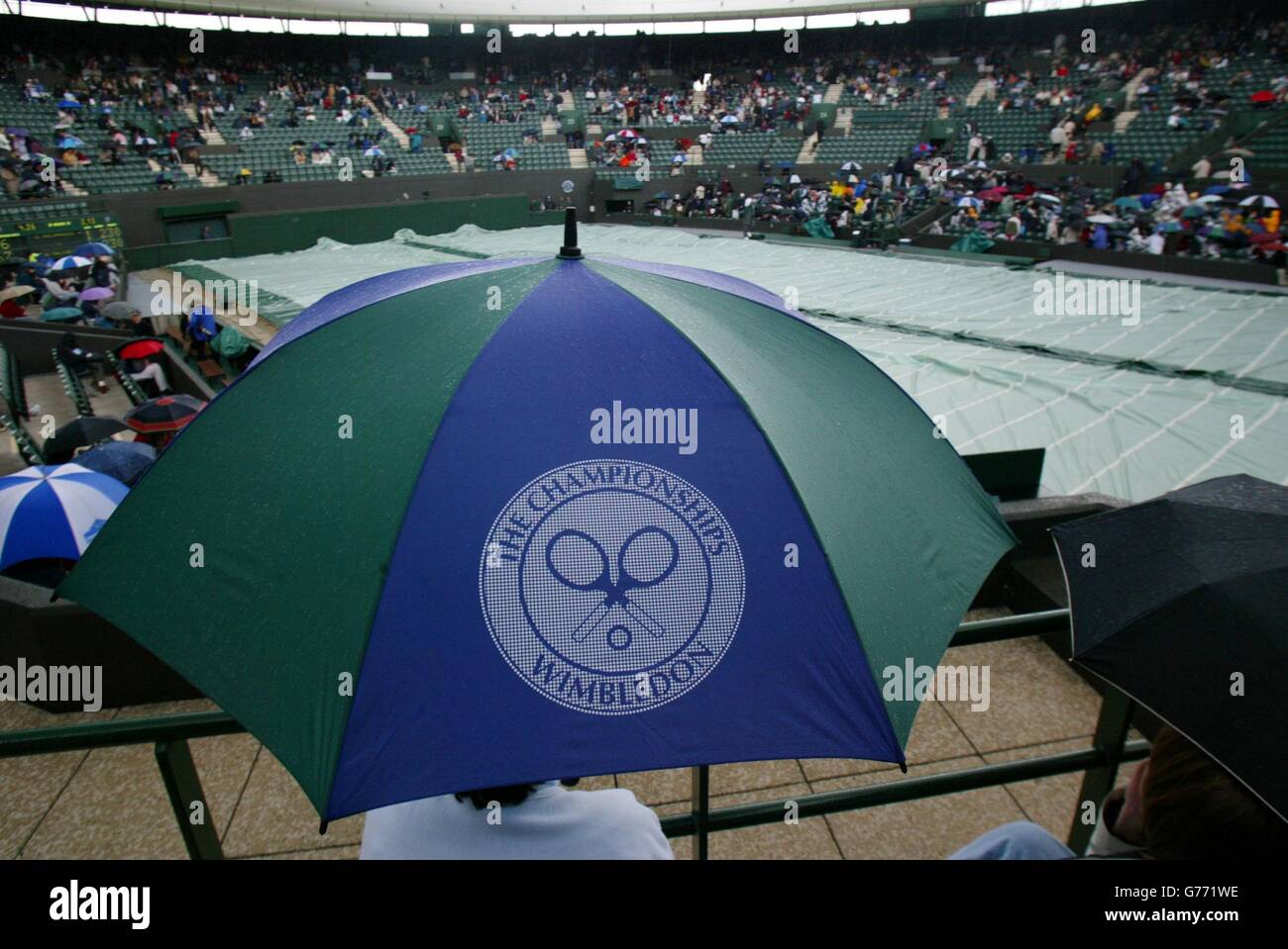 FÜR , KEINE KOMMERZIELLE VERWENDUNG. Tennis-Fans schützen sich vor dem Regen auf Court One während des Spiels zwischen Richard Krajicek aus den Niederlanden und Mark Philippoussis aus Australien in Wimbledon. Stockfoto