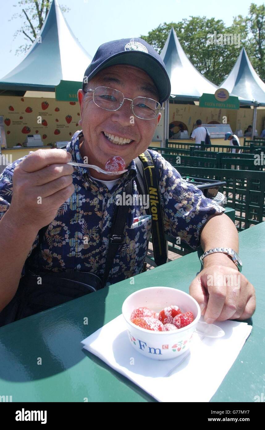 , KEINE HANDY-NUTZUNG. Ein Besucher der All England Lawn Tennis Championships in Wimbledon tuckt sich in die obligorischen Erdbeeren und Sahne. Stockfoto