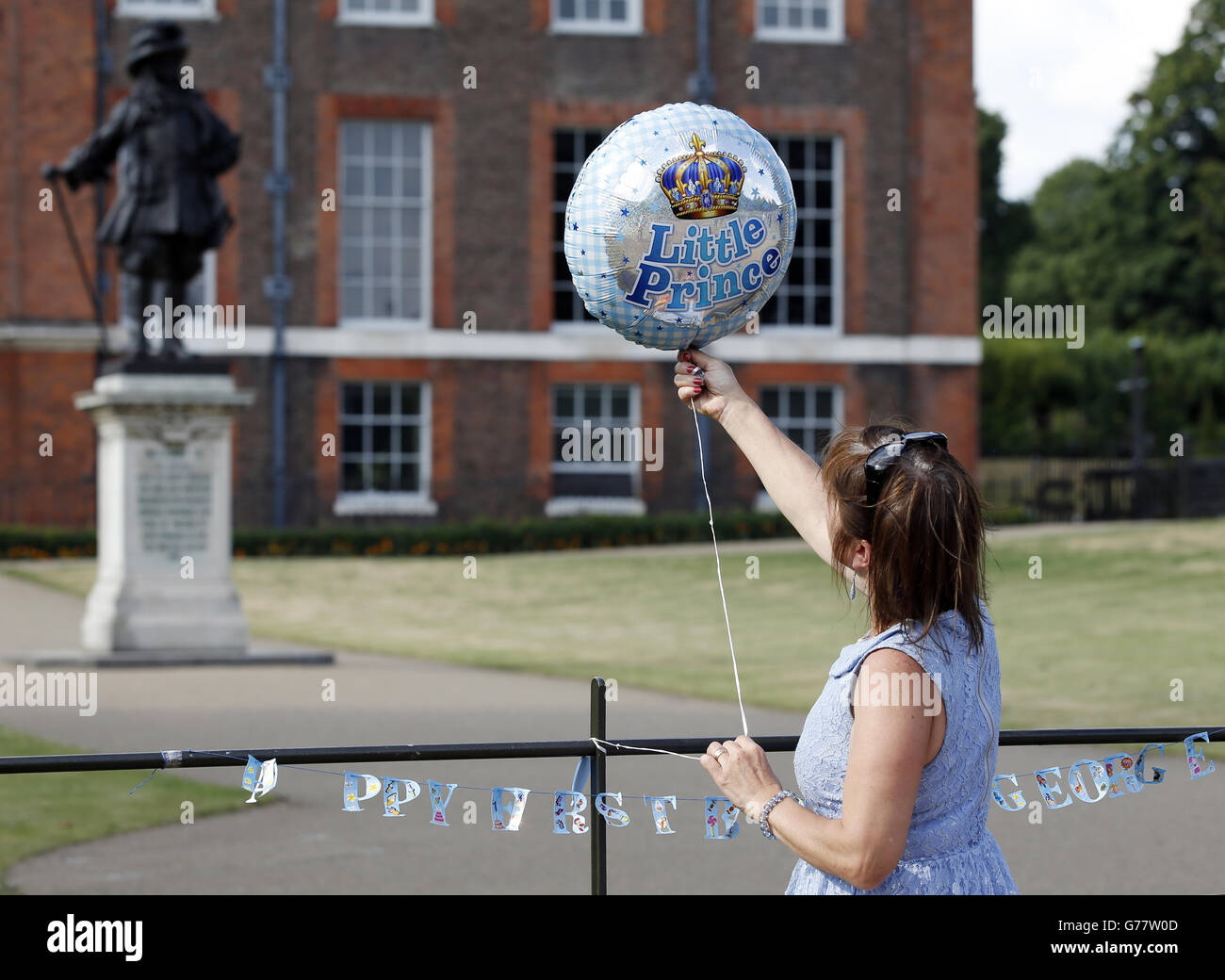 Kathy Martin aus Beckenham, Kent, bindet einen Ballon an Geländer vor den Toren des Kensington Palace, London, zur Feier des ersten Geburtstages von Prinz George. Stockfoto
