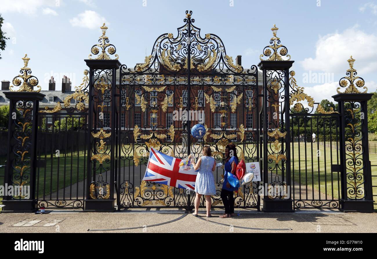 Teba Diatta (rechts) aus York, die einen Kuchen mitgebracht hat, und Kathy Martin aus Beckenham, Kent, die einen Ballon mitgebracht hat, stehen vor den Toren des Kensington Palace, London, zur Feier des ersten Geburtstages von Prinz George. Stockfoto