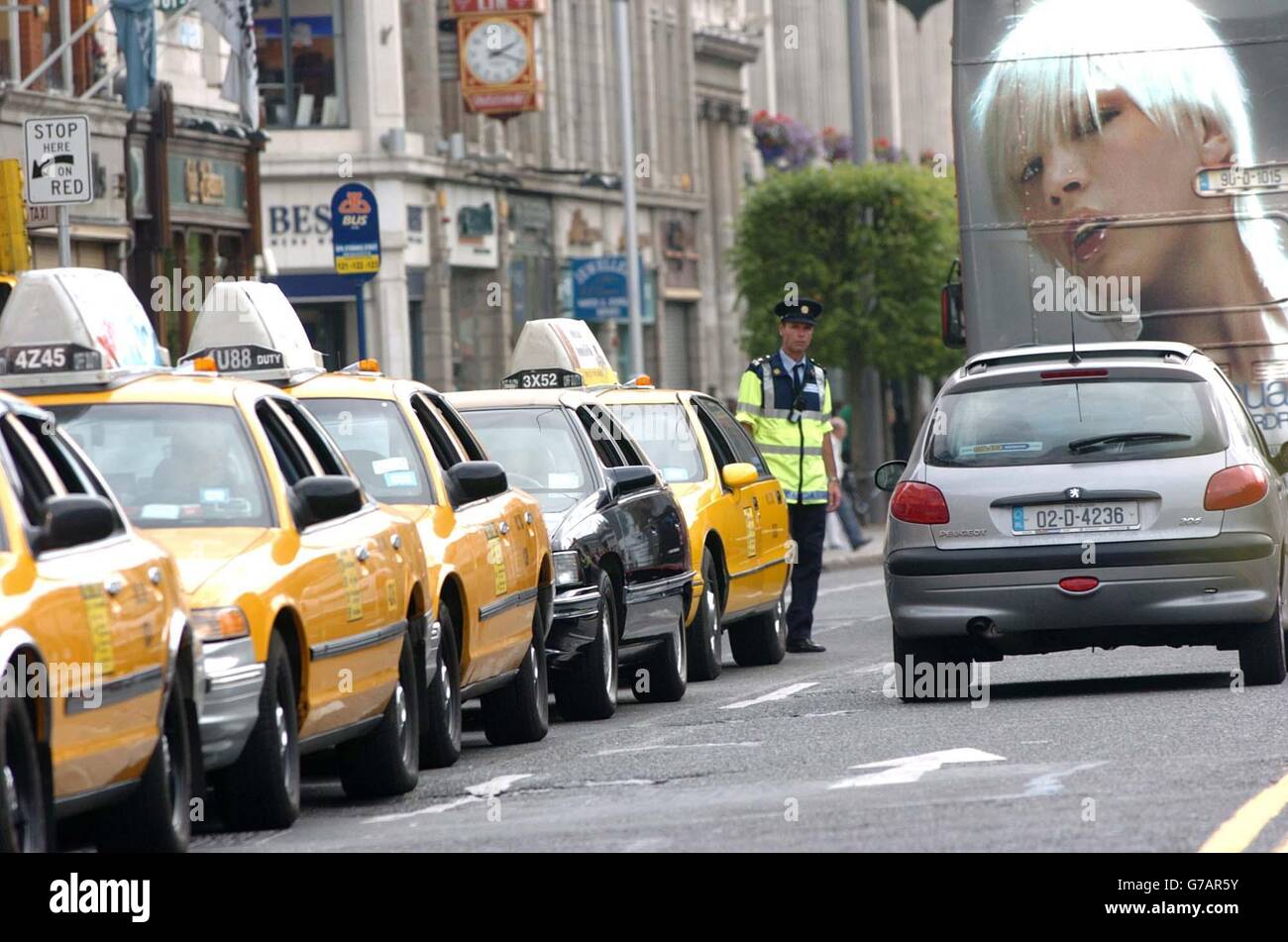 Ein Garda hält den Verkehr im Auge, der an geparkten gelben Taxis im US-Stil vorbeifährt, und zwar an der Filmkulisse einer Nachstellung von "The Honeymooners" in der O'Connell Street, Dublin, Irland. Hunderte von Menschen versammelten sich, um zu beobachten, wie die Gegend von Set-Bauherren und Requisiten verwandelt wurde, um wie eine typische Straße in den USA auszusehen. Stockfoto