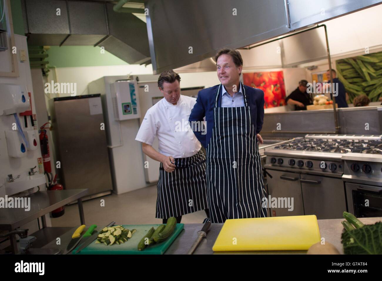 Der stellvertretende Premierminister Nick Clegg legt mit Hilfe von Mark Stower, Director of Food and Service, Harrison Catering Services, eine Schürze an, während er die Clapham Manor Primary School im Südwesten Londons besucht. Wo er offiziell das Programm der Regierung einführte, 5-7-Jährige mit kostenlosen Schulmahlzeiten zu versorgen. Stockfoto