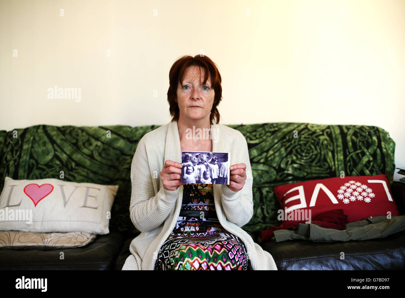 Missbrauchsuntersuchung gemäß NI. Missbrauch-Überlebende Kate Walmsley in ihrem Haus in Belfast mit einem Foto, das Kinder in einem Wohnhaus in Londonderry zeigt, mit Kate (vorne links) und Margaret McGuckian, Gründerin von Überlebenden und Opfern von institutionellem Missbrauch (zweite rechts). Stockfoto