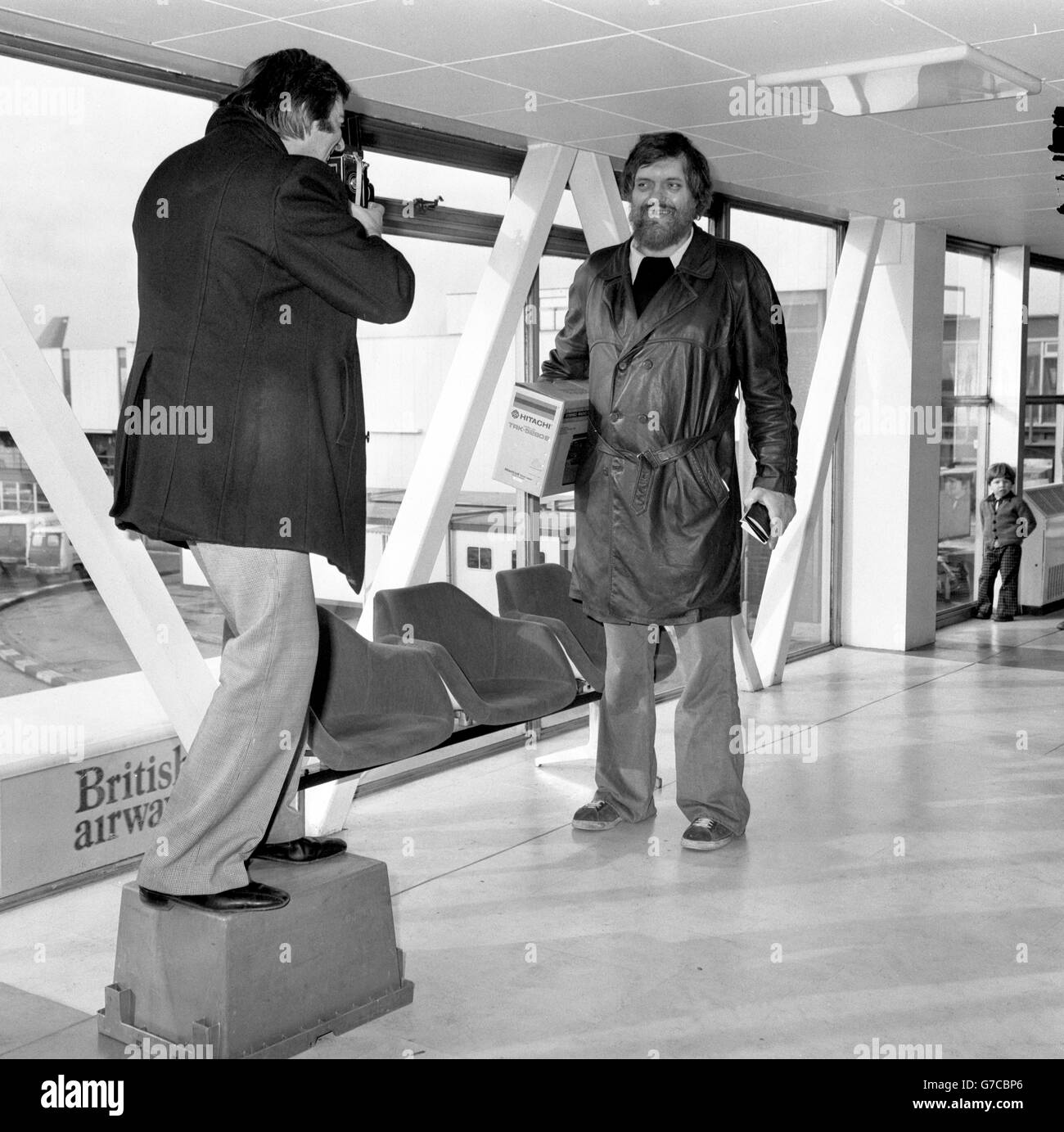 Ein Fotograf steht auf einer Kiste, um ein Foto des 7 m2 großen Schauspielers Richard Kiel am Flughafen Heathrow, London, zu machen. Er ist seit drei Wochen in Großbritannien, um Force 10 von Navarone zu schießen. Stockfoto