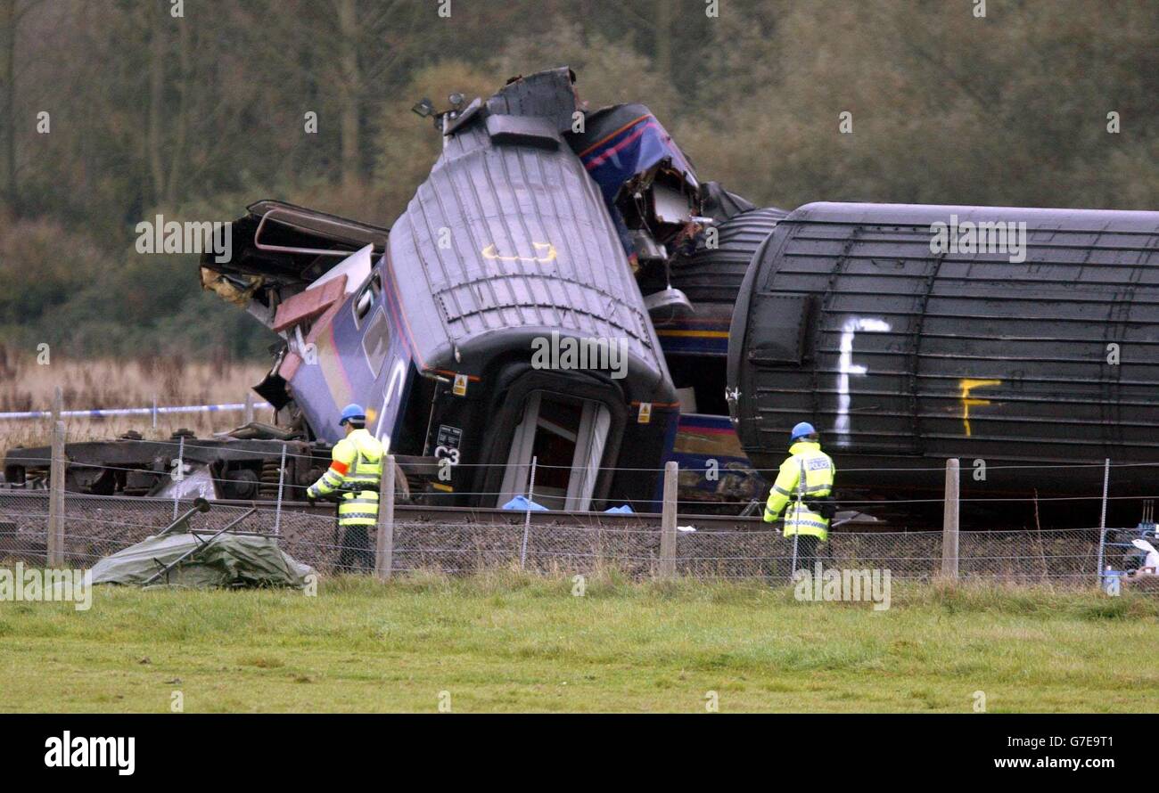 Beamte gehen an dem Zug vorbei, der am Samstag auf einem abgelegenen Bahnübergang in der Nähe von Ufton Nervet in Berkshire mit einem Limousine fuhr. Sechs Menschen starben bei dem Einschlag und ein Siebter starb am Sonntag im Krankenhaus. Die Polizei, die den Vorfall untersucht, konzentriert sich darauf, warum ein Autofahrer sein Auto in den Weg des Zuges geparkt hat. Alle Leichen wurden nun von der Baustelle entfernt und ein Kran wird gebaut, um das Wrack zu räumen. 06/12/2004 die Multi-Millionen-Pfund-Rechnung für den Crash, der sieben Menschen getötet und Dutzende verletzt, wird aus einem Cash-Pot von der Versicherungsbranche von Fahrern finanziert bezahlt werden Stockfoto