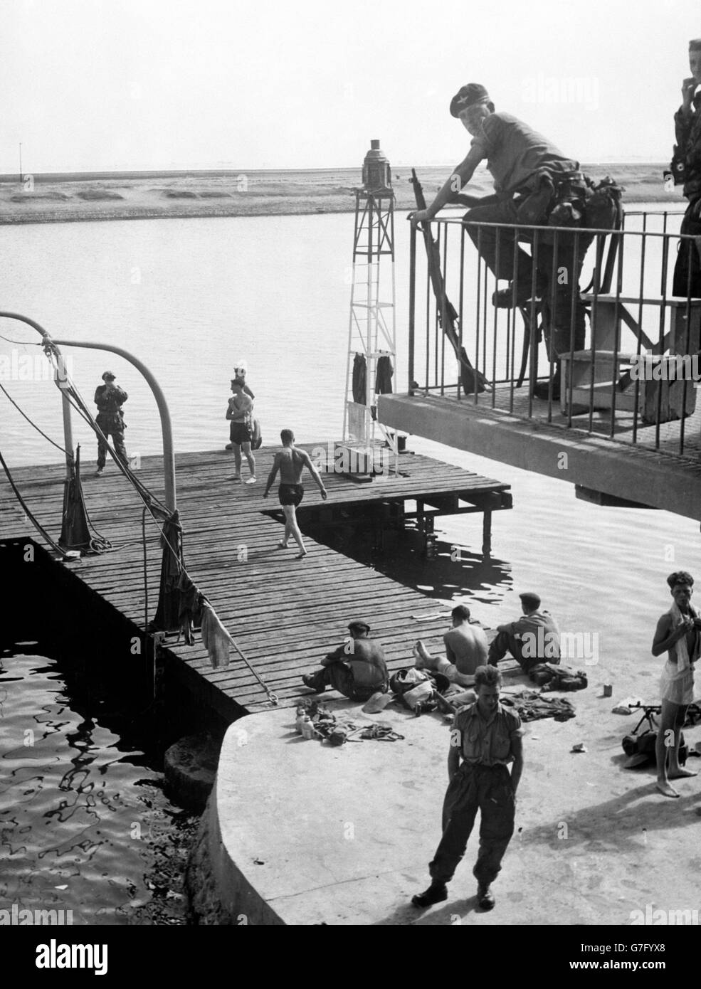 Ein bewaffneter Wachposten wacht von oben, wenn britische Soldaten der anglo-französischen Streitkräfte vom Anlegesteg der Suez Company im Suezkanal baden. Stockfoto