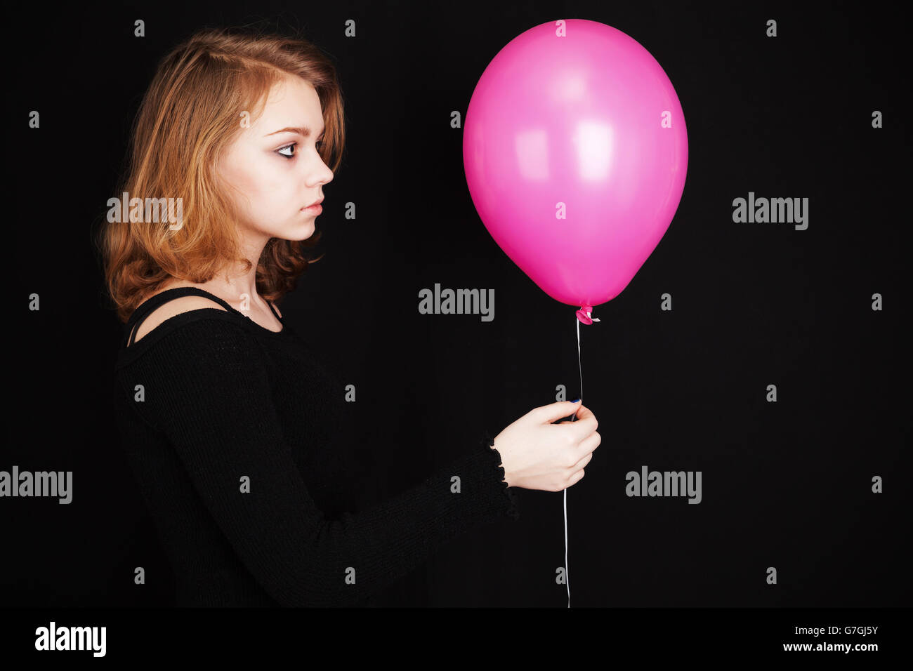 Studio-Profil-Porträt des blonden Mädchens mit rosa Ballon über schwarzen Hintergrund Stockfoto