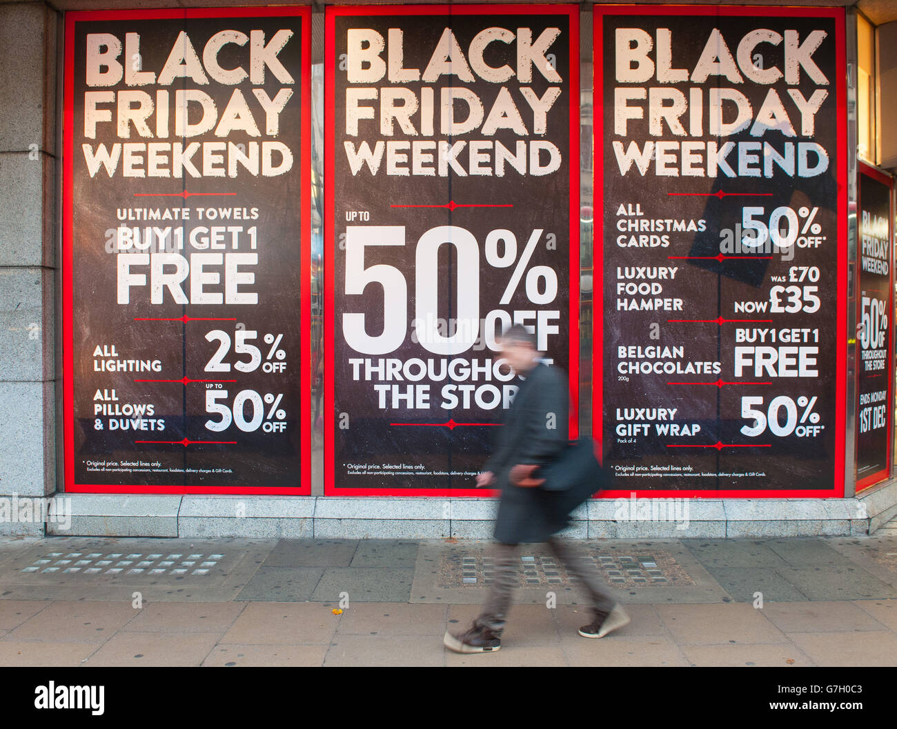 Die Leute kommen an Plakaten vorbei, die auf der Oxford Street, London, für den Verkauf des "Black Friday" werben. Stockfoto
