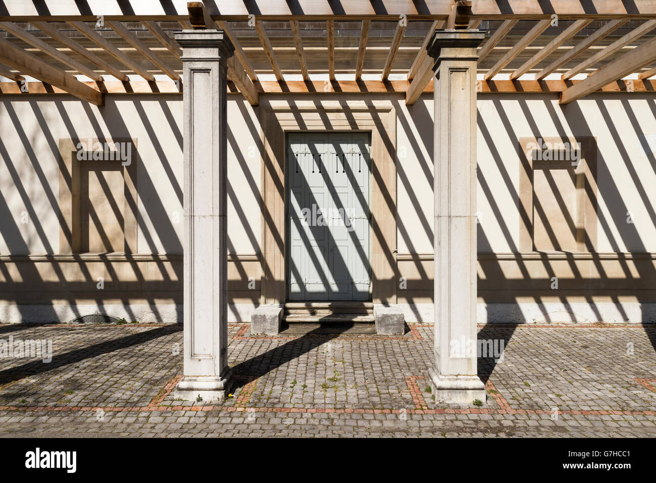 Vorderansicht auf den Seiteneingang einer alten Villa mit einer Pergola. Die starke Sonneneinstrahlung wirft dunkle Schatten Streifen auf das Gebäude Stockfoto