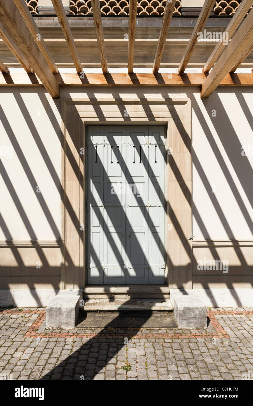Vorderansicht auf den Seiteneingang einer alten Villa mit einer Pergola. Die starke Sonneneinstrahlung wirft dunkle Schatten Streifen auf das Gebäude Stockfoto