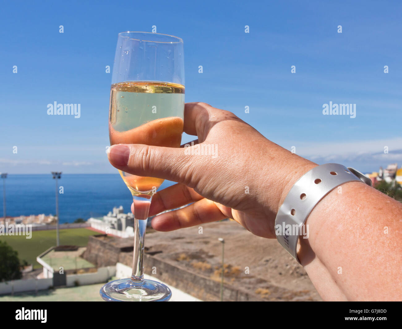 All-Inclusive-Armband am weiblichen Handgelenk, sonnigen Urlaub, Glas Weißwein, Atlantik, Urlaub auf Teneriffa Stockfoto