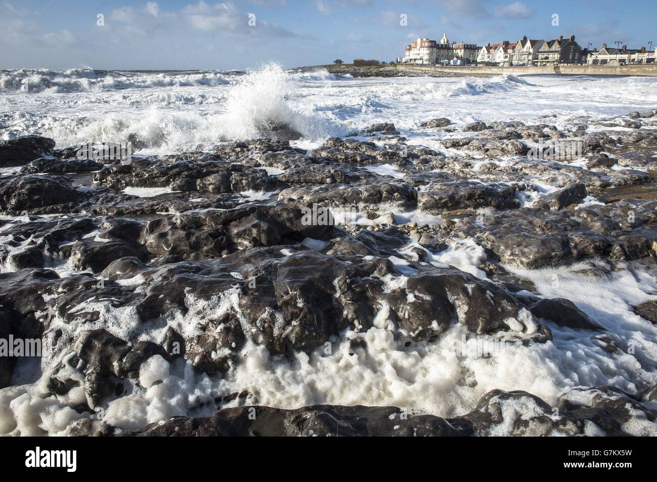 Wellen brechen und Schaum bläst um Felsen am Porthcawl Beach, Wales, wo der Wind mit härterem Wetter aufgeholt hat, da er für den Rest der Woche geschlossen wird. Stockfoto