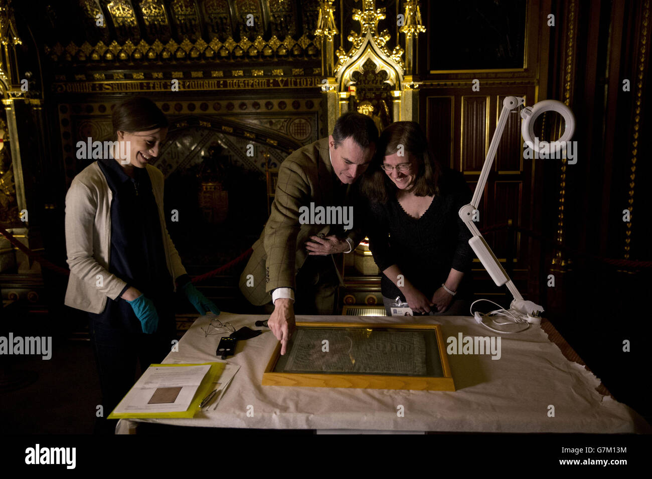 Die Salisbury Cathedral 1215 Kopie der Magna Carta wird von (von links nach rechts) Parlamentarischer Archivkonservatorin Oriana Calman, Chris Woods, dem Direktor des National Conservation Service und Salisbury Cathedral Archivarin Emily Naish, Bevor er in einem Kabinett aufgestellt wurde, das neben den anderen drei erhaltenen OriginalPergamentfesseln der Magna Carta anlässlich des 800. Jahrestages der Versiegelung von Magna Carta in Runnymede im Jahr 1215 im Robing Room der Queen im Houses of Parliament in London ausgestellt werden soll. Stockfoto