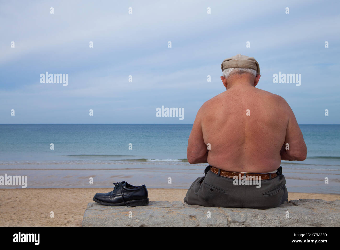Alter Mann sitzt allein am Strand Stockfoto