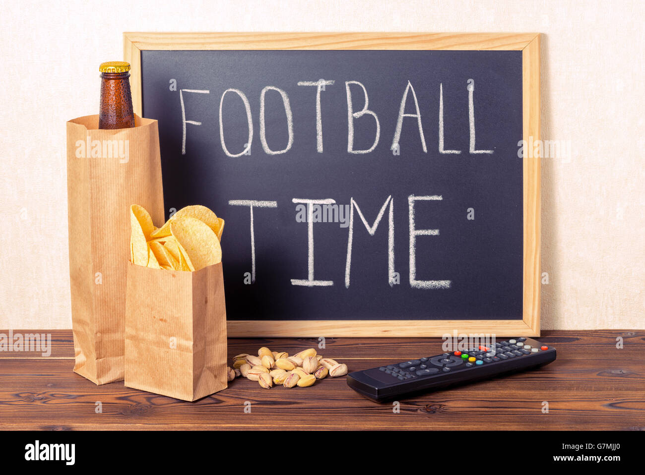 Fußball-Fans-Konzept der Bierflasche in braune Papiertüte, Chips, Pistazie, TV-Fernbedienung und Handschrift Text Fußball Zeit Stockfoto