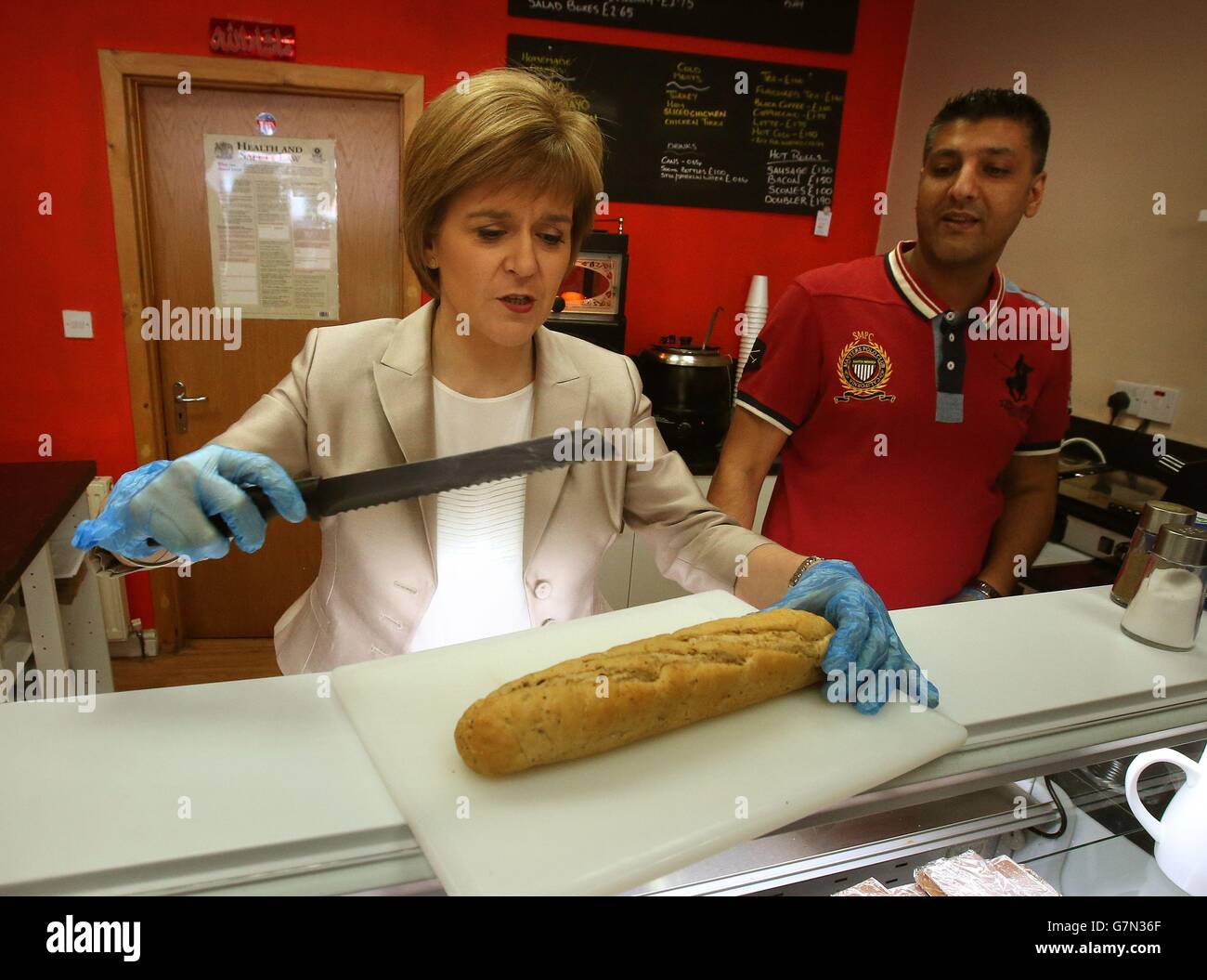 SNP-Leiterin und erste Ministerin Nicola Sturgeon macht ein Sandwich in der Quick Bite Sandwich Bar in Glasgow mit Besitzer Aftab Baig, während sie mit lokalen Aktivisten kämpft. Stockfoto