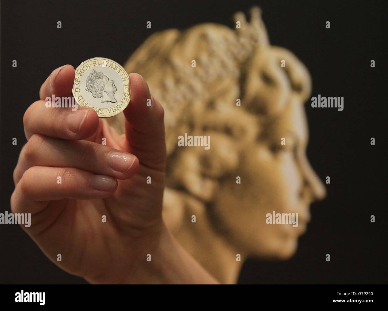 Ein Event-Assistent der Royal Mint hält eine neue zwei-Pfund-Münze vor dem Münzporträt von Arnold Machin von Königin Elizabeth II. Während einer Enthüllungszeremonie für das neueste Münzportrait von Königin Elizabeth II. In der National Portrait Gallery, London. Stockfoto