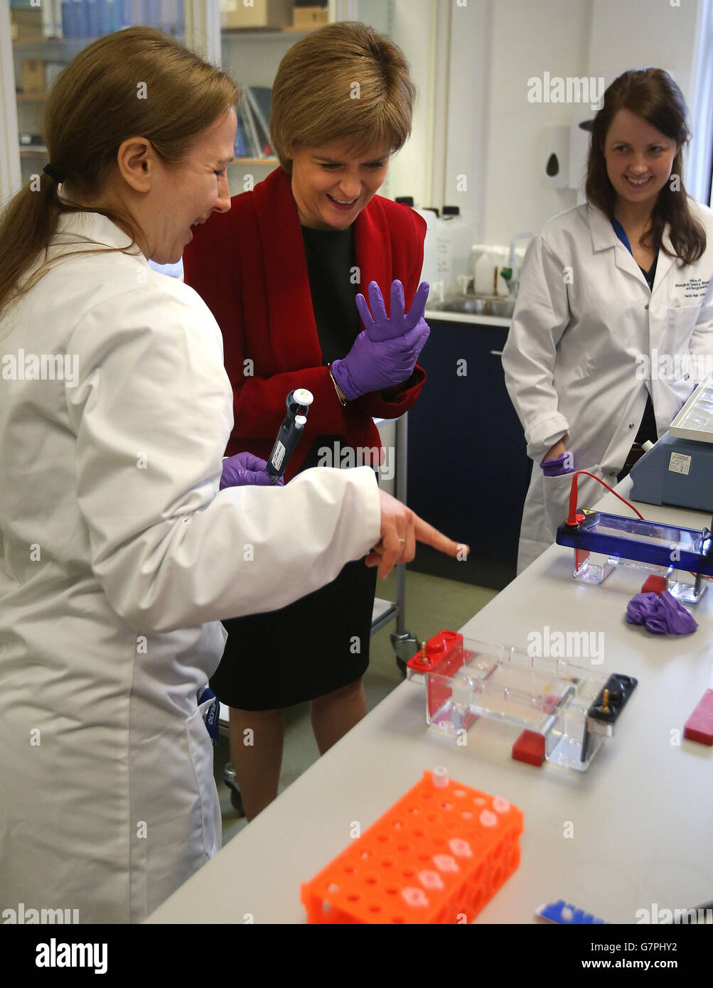 Die erste Ministerin Nicola Sturgeon lädt ein DNA-Gel, das von der Doktorandin Alicja Graczyk (links) und Deirdre Kavanagh (rechts) Post Doc Researcher während eines Besuchs im Heriot-Watt Life Sciences Laboratory an der Heriot-Watt University nach einer Einweisung in die Publikation Government Expenditing and Revenue Scotland (2013-14) beobachtet wurde. Stockfoto