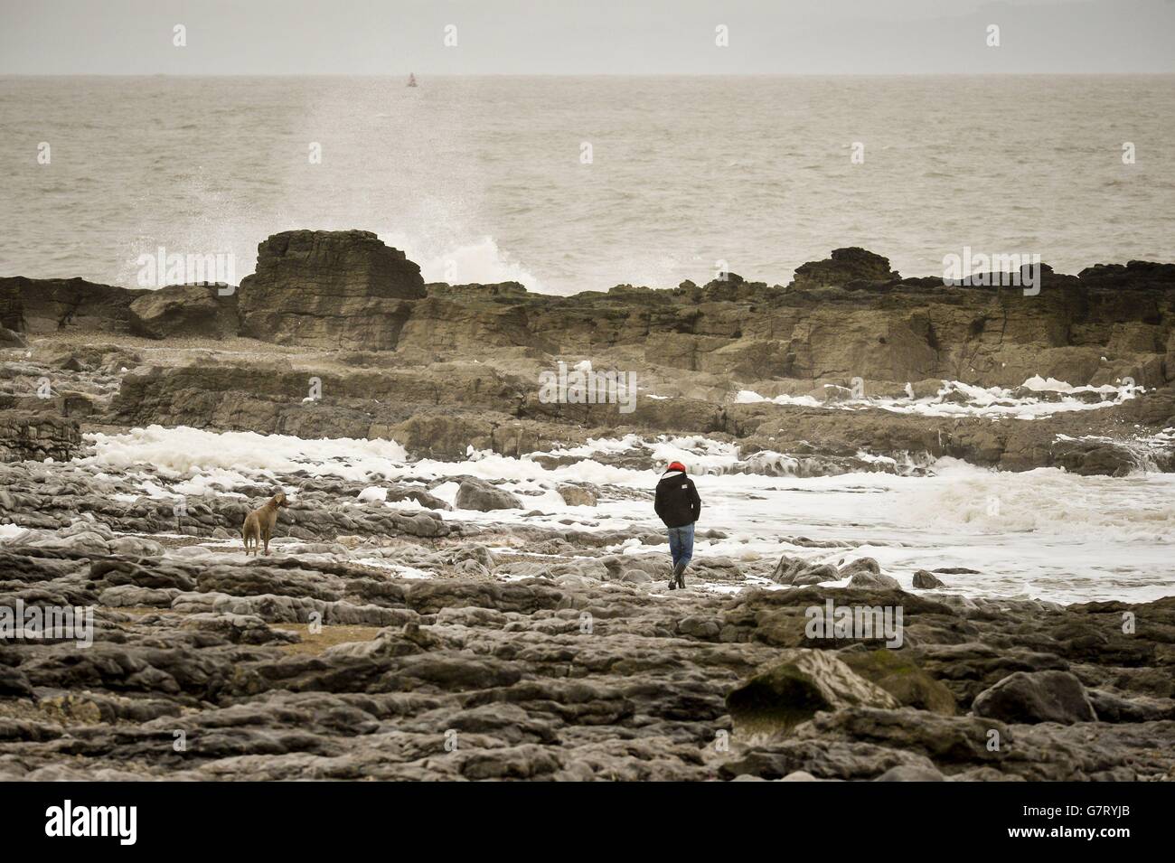 Ein Mann geht mit seinem Hund am Porthcawl Beach in Südwales, während Stürme und sintflutartige Regenfälle in Großbritannien in einer weiteren Wetterexplosion vor Ostern über die Stadt ziehen werden. Stockfoto
