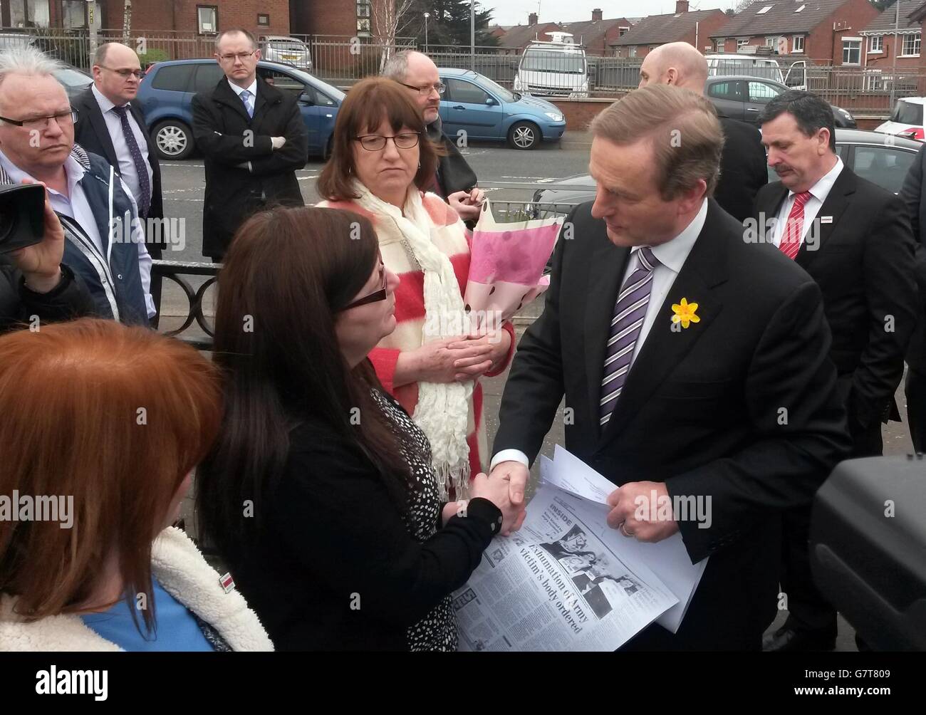 Enda Kenny schüttelt sich die Hände mit Janet Donnelly, Tochter des Ballymurphy-Erschießungsopfer Joseph Murphy, als er die Szene der Morde im Westen Belfasts besucht. Stockfoto