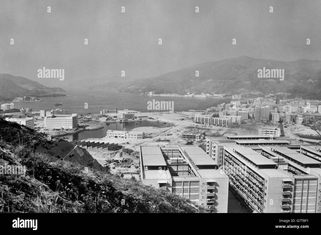 Die neue Wohnanlage wurde teilweise in Tsuen Wan fertiggestellt, die der Eckstein des Kwai Chung-Bauvorhaben sein wird. Im Vordergrund (rechts) befinden sich Umsiedlungshäuser, die auf terrassenförmigem Land gebaut wurden und auf der linken Seite neue Fabriken, die auf Land errichtet wurden, das aus dem Meer zurückgewonnen wurde. Stockfoto