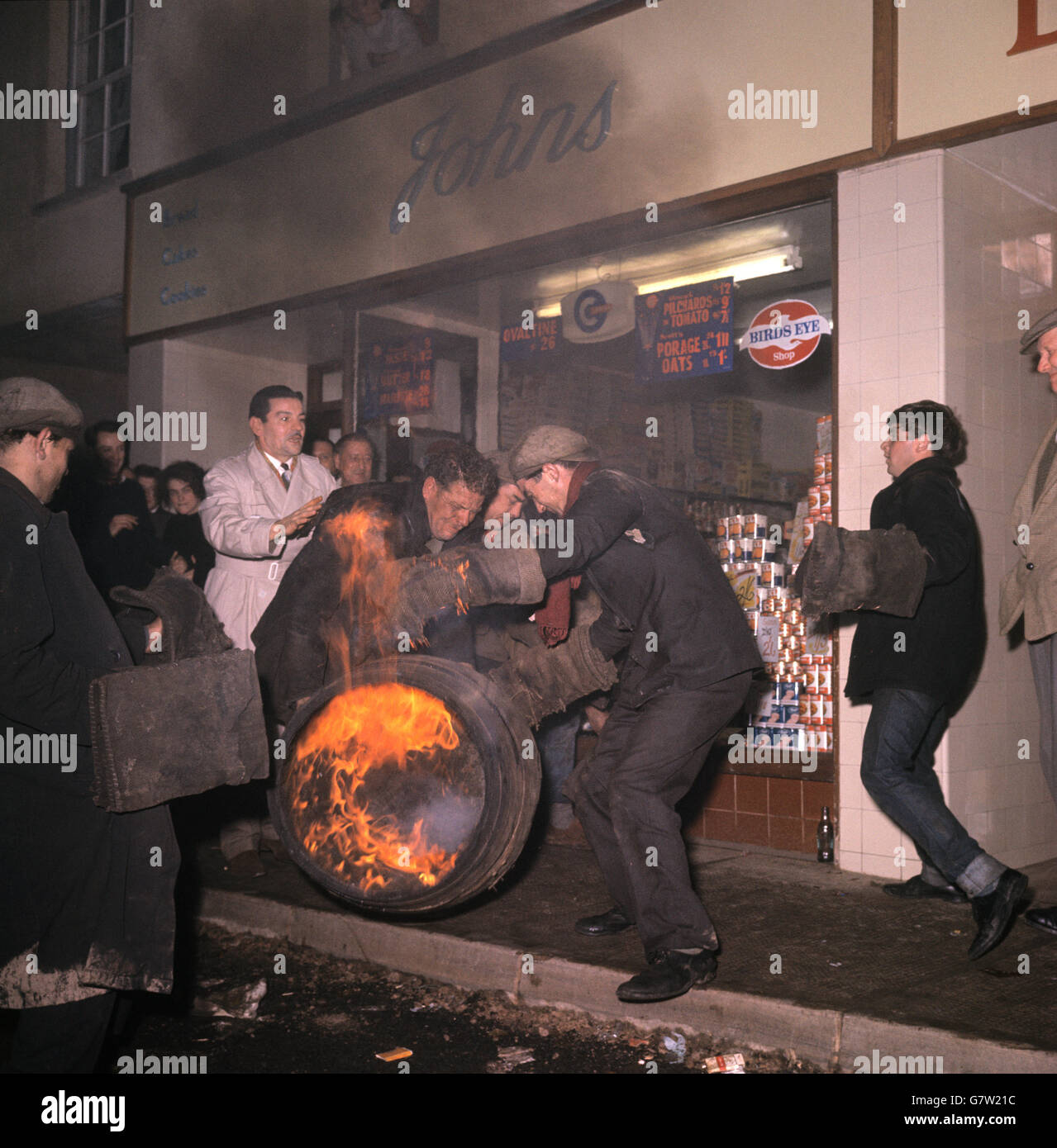 Ein Mann versucht, sich mit einem brennenden Fass auf der Straße auseinanderzusetzen, während andere darauf schauen. Stockfoto